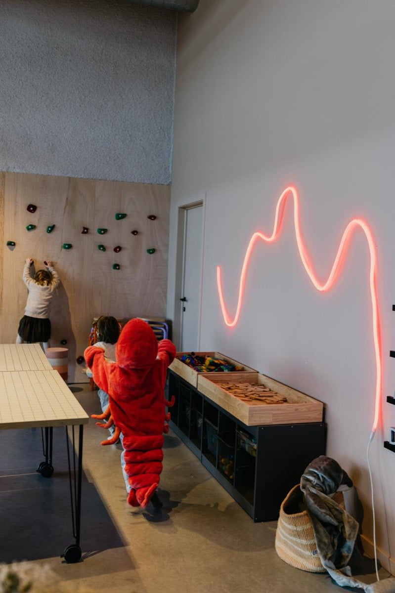 Een kind in een kreeftenpak loopt langs de speelhoek met neonlicht