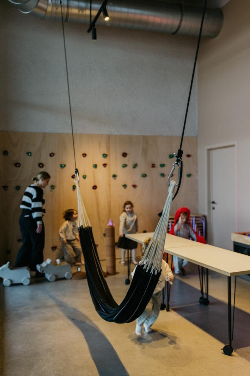 Kinderen spelen met de oppas bij de klimmuur en de hangmat