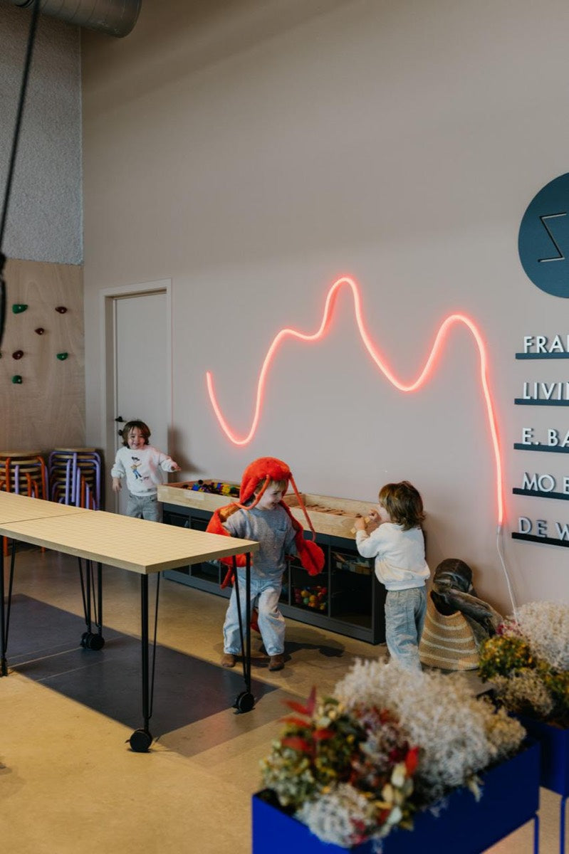 Kinderen spelen in de speelhoek terwijl de mama's aan tafel zitten